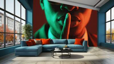 Shush gesture. Man secret. Confidential conspiracy. Green red neon light unrecognizable gentleman in suit glasses warning shh with finger on lips on dark. Wall mural