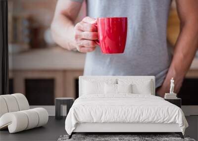 traditional morning hot beverage. quick and easy breakfast. man holding tea or instant coffee drink in a red mug standing in the kitchen. Wall mural