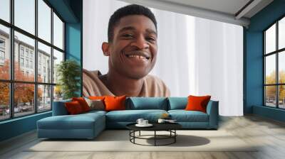 Video call. Virtual meeting. Positive attitude. Joyful optimistic cheerful young man in good mood with happy toothy smile at window copy space. Wall mural