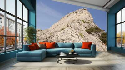 View from below on a high mountain, illuminated by the bright sun, directed into the blue sky. Wall mural