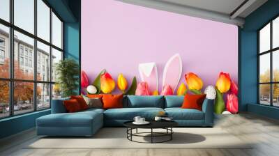 Easter concept. Top view photo of rabbit bunny ears colorful easter eggs and tulips flowers on isolated lilac background with empty space Wall mural