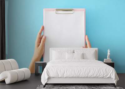 International Hepatitis Day concept. First person top view of female hands holding clipboard organizer on pastel blue background with empty space for message Wall mural