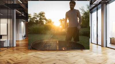 Lifestyle. Family barbecue outdoors. Young caucasian man getting the fire ready for grilling in the garden at sunset.  Wall mural