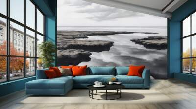 A serene seascape with rocky formations and a cloudy sky reflected in the calm water. Wall mural