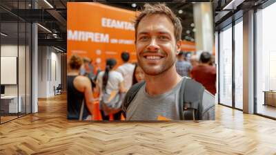 A cheerful man at an event with an orange backdrop smiling at the camera. Wall mural