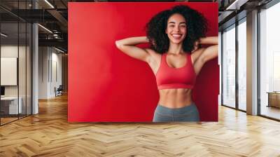 Smiling woman in red sports bra against red backdrop. Wall mural