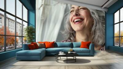 Woman with gray hair laughing near white curtains happily. Wall mural