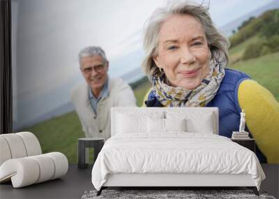  Healthy senior woman holding husband's hand and leading way on countryside walk Wall mural