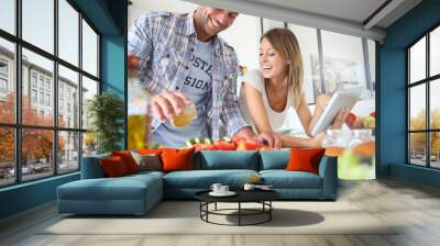 Cheerful couple in kitchen cooking dinner, using tablet Wall mural