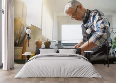 Cheerful mature man in kitchen preparing dish Wall mural