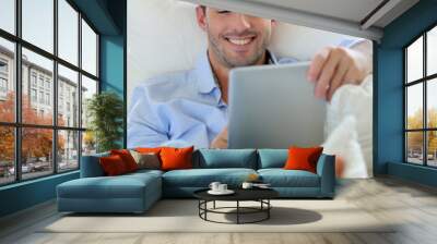 Cheerful young man laying in sofa with digital tablet Wall mural