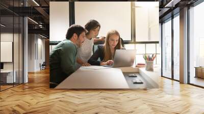 Group of three co workers looking over computer in modern workplace Wall mural