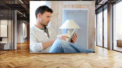 Handsome man relaxing at home with digital tablet Wall mural