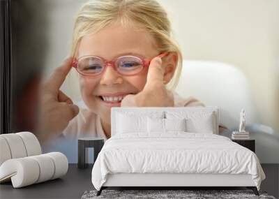 Little girl at the optician trying different eyeglasses Wall mural