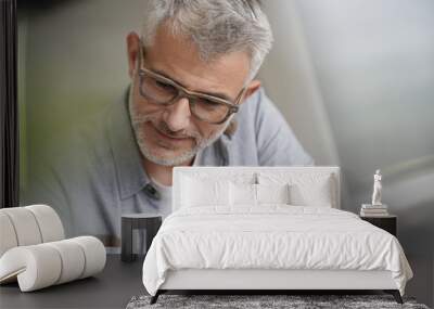 Middle-aged guy with trendy eyeglasses reading magazine Wall mural