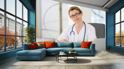 Portrait of mature nurse sitting at desk in office Wall mural