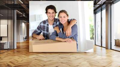 Smiling couple leaning on boxes in new home Wall mural