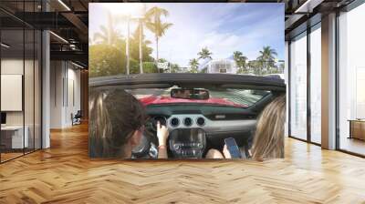 Two friends driving through sunny city in convertible car Wall mural