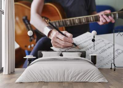 a person making notes on sheet music and holding a guitar. Wall mural