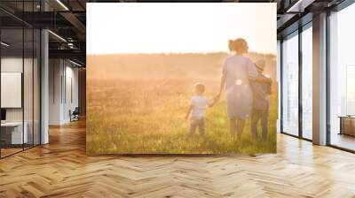 Beautiful young woman with two boys on the daisy meadow on a sunny day. Happy family on summer sunset. Kid boy, toddler and mom. Mum with baby and kid. Family and lifestyle concept Wall mural