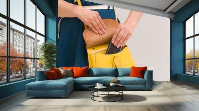 Closeup of woman's hands taking out smartphone from yellow purse. Image of young stylish woman taking cellphone out of handbag. Girl with phone. Communication and lifestyle concept Wall mural