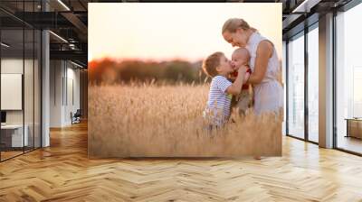 happy family enjoying sunset in wheat field. beautiful young woman with adorable baby boy and kid bo Wall mural