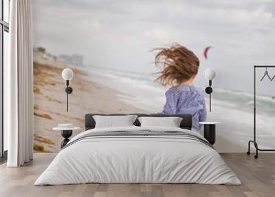 Little girl running on the ocean beach on a cloudy day. Vacation by the sea. Cute kid girl on the deserted beach. Summer, outdoors. Wind in the hair of a small girl. Beach landscape. Wall mural