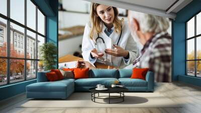 Female doctor measuring blood pressure of a senior man during a home visit Wall mural