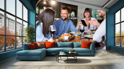 Group of happy business colleagues using cell phone during lunch in a restaurant Wall mural