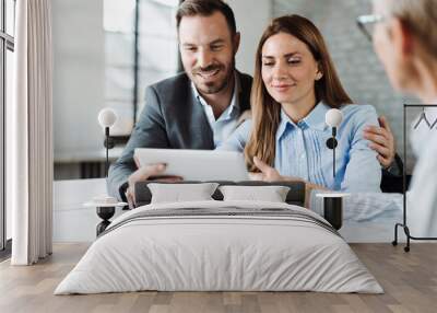 Happy couple using digital tablet while having a meeting with their insurance agent in the office Wall mural