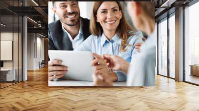 Happy couple using digital tablet while having a meeting with their insurance agent in the office Wall mural