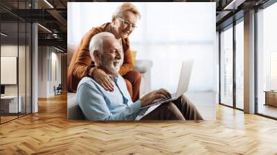 Senior couple surfing the Internet on their laptop at home Wall mural