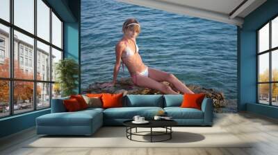 Teenage girl in bikini sitting on a rock in the sea Wall mural