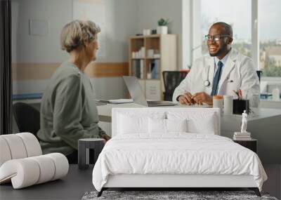 African American Family Doctor is Prescribing Medication to Senior Female Patient and Speaking with Her During Consultation in a Health Clinic. Physician Sitting Behind a Desk in Hospital Office. Wall mural