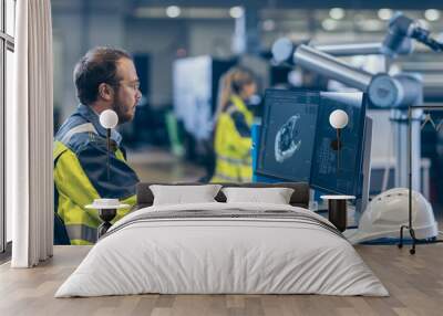 At the Factory: Mechanical Engineer Works on Computer, Designs in CAD 3D Model of the Engine. In the Background Factory Workers and Functioning Robotic Arm. Wall mural