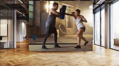 Athletic Woman Hits Punching Bag that Her Partner/ Trainer Holds. She's Professional Fighter and is Training in a Gym. Wall mural