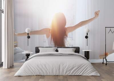 Beautiful Brunette is Waking up in the Morning, Stretches in the Bed, Sun Shines on Her From the Big Window. Happy Young Girl Greets New Day with Warm Sunlight Flare. Wall mural