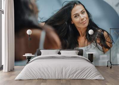 Beautiful Early Middle Aged Woman Looks into Bathroom Mirror Touches Her Lush Black Hair, Admires Her Looks. Concept for Happiness, Wellbeing, Natural Beauty, Organic Skin Care Products Wall mural