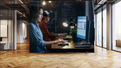 beautiful female coder works at her desktop on her peropnal computer. her male colleague sits next t Wall mural