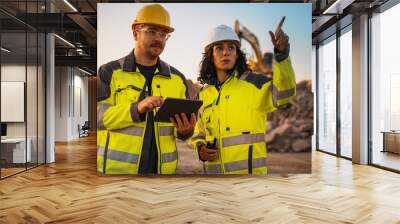 Caucasian Male Civil Engineer Talking To Hispanic Female Inspector And Using Tablet Computer On Construction Site of New Building. Real Estate Developers Discussing Business, Excavators Working. Wall mural