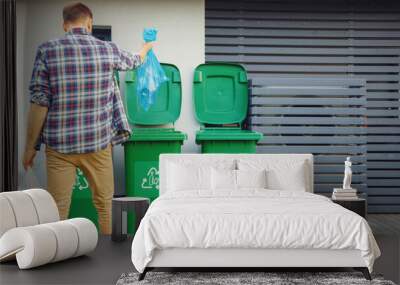 Caucasian Man is Throwing Away Two Plastic Bags of Trash next to His House. One Garbage Bag is Sorted with Biological Food Waste, Other with Recyclable Bottles Garbage Bin. Wall mural