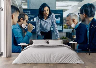 Chief Female Executive Leans and Spreads Project Blueprints on the Table Showing them to Her Colleagues. In the Background Pie Charts and Company's Growth on the Wall TV. Wall mural