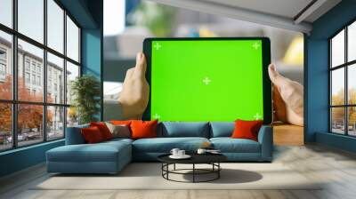 Close-up of Man Using Green Mock-up Screen Digital Tablet Computer in Landscape Mode while Sitting at His Desk. In the Background Cozy Living Room. Wall mural