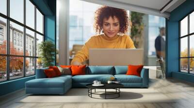 Close Up Portrait of a Happy Middle Eastern Manager Sitting at a Desk in Creative Office. Young Stylish Female with Curly Hair Using Laptop Computer in Marketing Agency. Wall mural