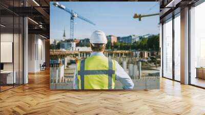 Confident Bearded Head Civil Engineer-Architect in Sunglasses is Standing Outside with His Back to Camera in a Construction Site on a Bright Day. Man is Wearing a Hard Hat, Shirt and a Safety Vest. Wall mural