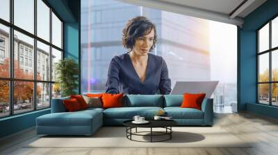 Confident Businesswoman Sitting at Her Desk and Working on a Laptop in Her Modern Office. Stylish Beautiful Woman Doing Important Job. In the Window Big City Business District View with Sun Flare.  Wall mural