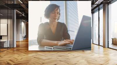 Confident Businesswoman Working on a Laptop in Her Modern Office. Stylish Beautiful Woman Doing Important Job. In the Window Big City Business District View.  Wall mural