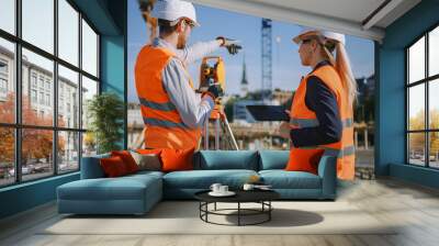 Construction Worker Using Theodolite Surveying Optical Instrument for Measuring Angles in Horizontal and Vertical Planes on Construction Site. Engineer and Architect Using Tablet Next to Surveyor. Wall mural