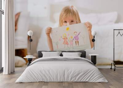 Cute Young Girl Sitting on Pillows and Shows Drawing of Her Family and Hides Behind It. Sunny Living Room. Wall mural