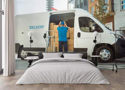 Delivery Man Uses Hand Truck Trolley Full of Cardboard Boxes and Packages, Loads Parcels into Truck / Van. Professional Courier / Loader helping you Move, Delivering Your Purchased Items Efficiently Wall mural